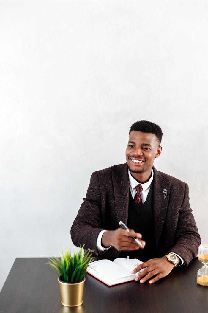 Confident businessman writing in a notebook at a desk, smiling and planning.