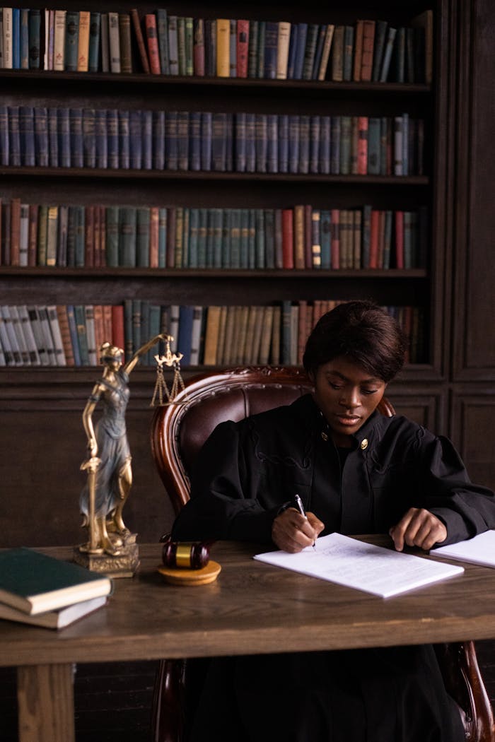 why-choose-us-01 Black female judge sitting at desk in library, writing legal documents.